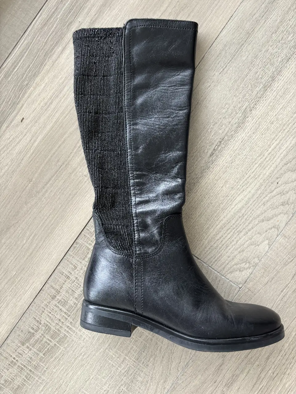 Botas de caña alta negras de cuero, con detalle de tejido elástico en la parte superior. Tienen cierre lateral y suela plana.