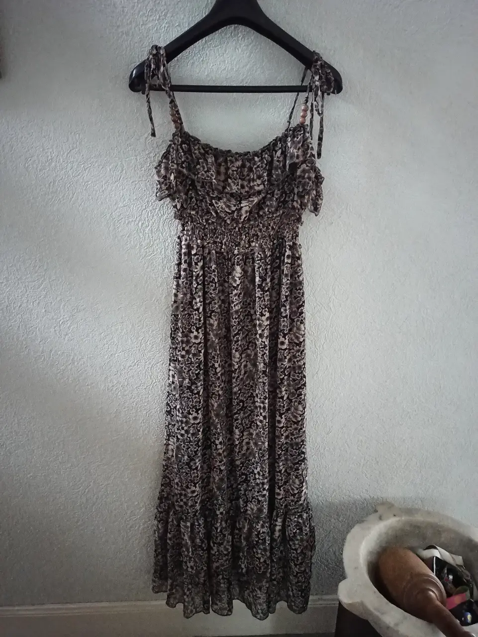 Vestido largo de mujer con estampado floral en tonos marrones y negros. Diseño con tirantes finos ajustables y detalle de volantes en el pecho. Ideal para un look bohemio y fresco.