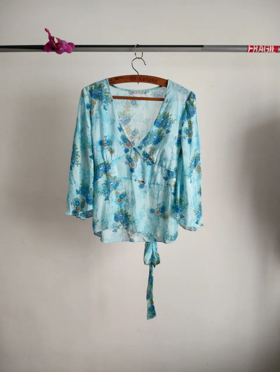 Blusa súper delicada y femenina con estampa floral en tonos celestes y azules. Posee mangas largas acampanadas abiertas y un lazo para atar en la cintura, lo que permite ajustar la prenda y crear un efecto entallado. Ideal para un look romántico y fresco.