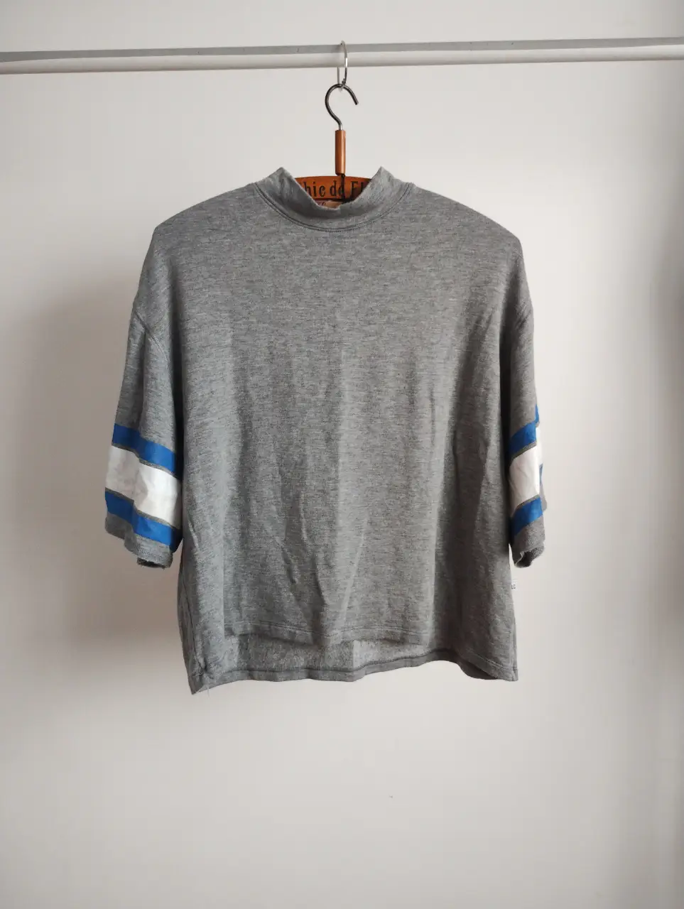 remera deportiva  gris de manga corta con detalles en azul y blanco en las mangas. Cuello alto. Ideal para un look casual y cómodo. frizado, calentito y cómodo