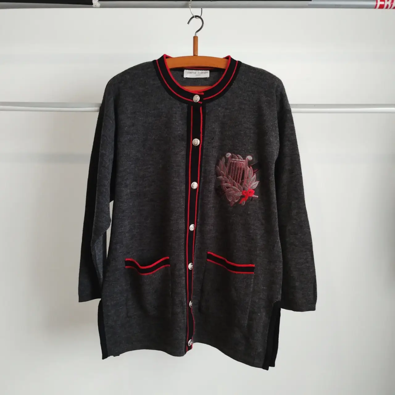 Cardigan gris de la marca Pierre Cardin, con detalles en rojo y negro. Presenta un bordado en el pecho y botones plateados. Ideal para un look elegante y vintage. 