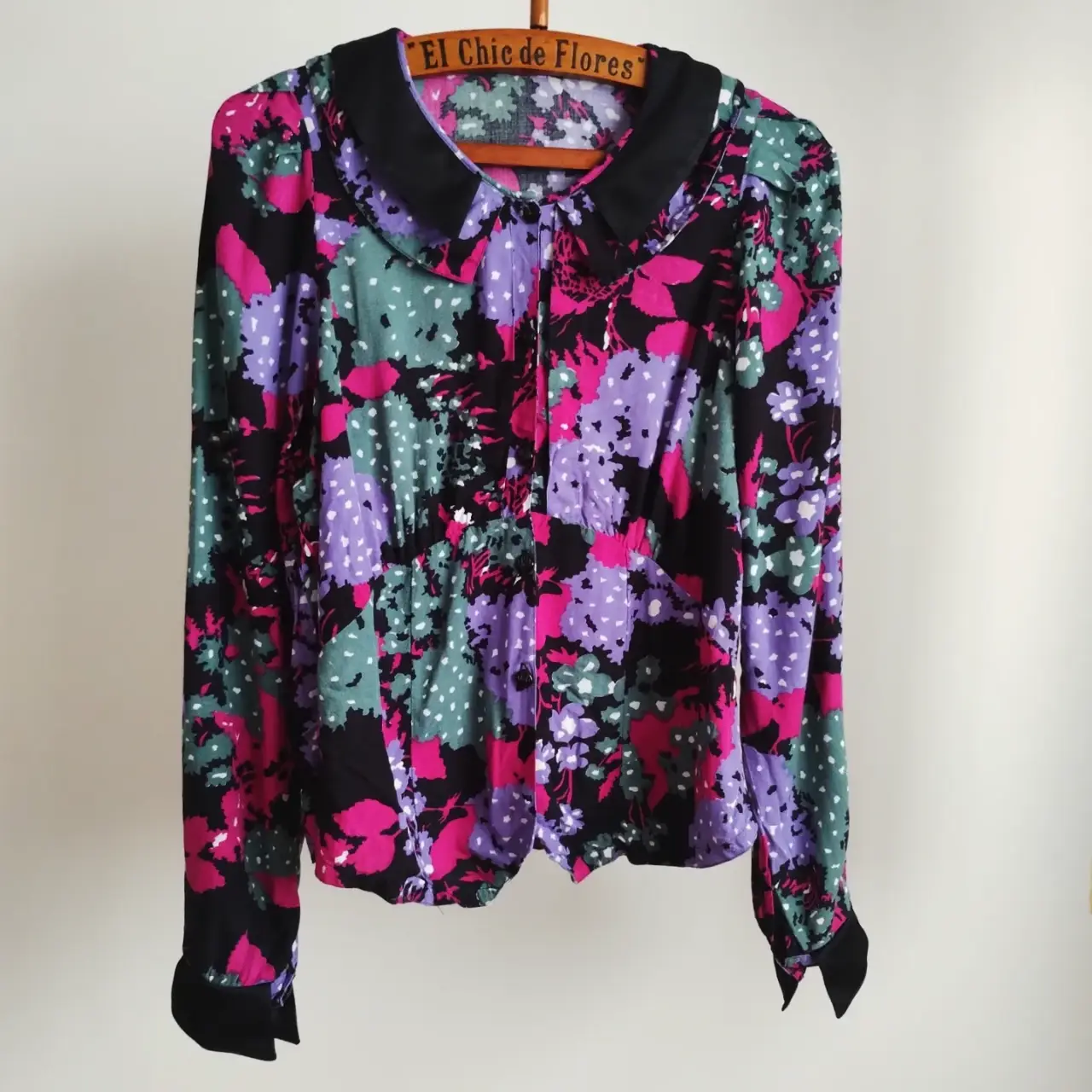 camisa vintage con estampado floral en tonos violetas, rosas y verdes sobre fondo negro. Cuello y puños negros. Ideal para un look retro y con estilo.