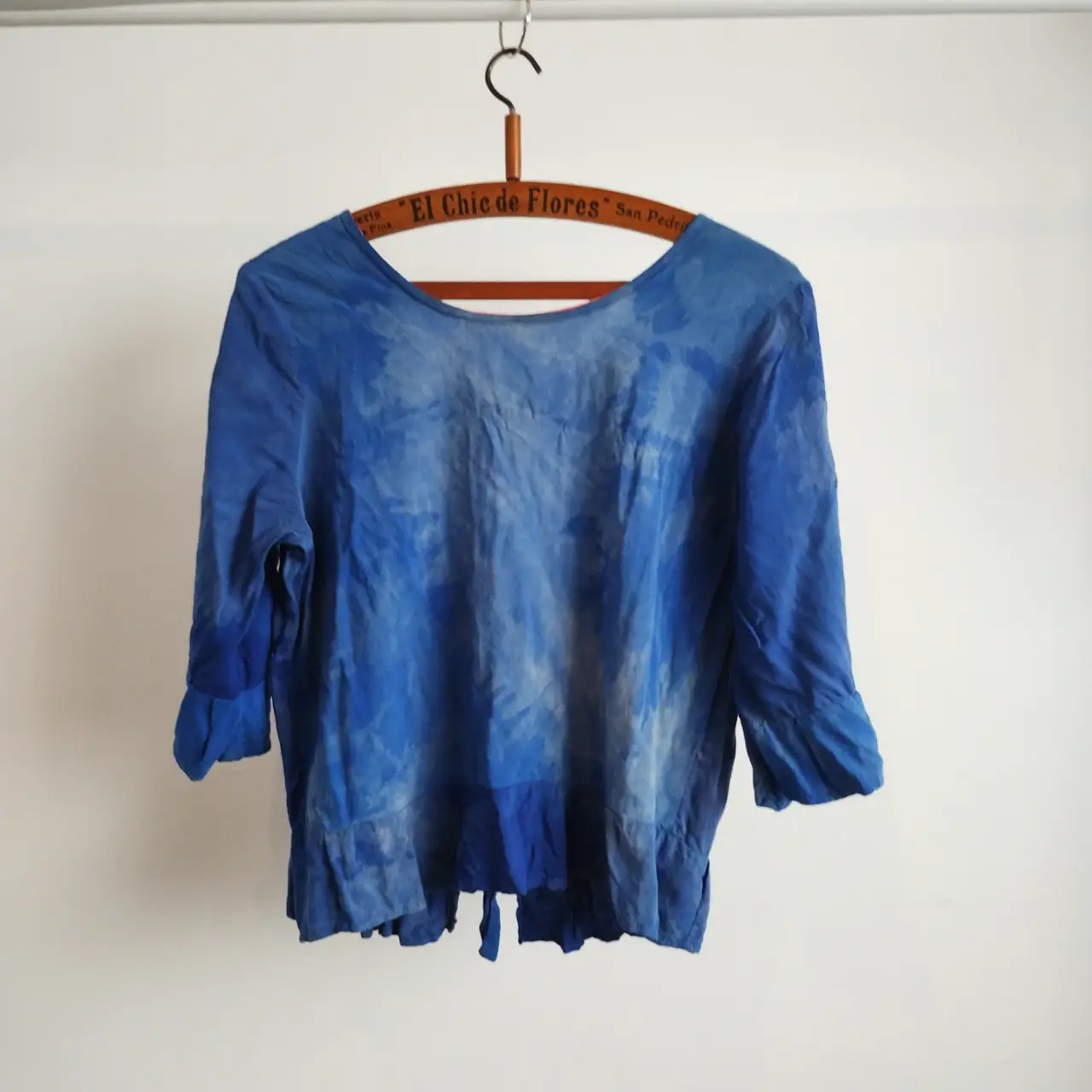 Blusa de algodón/fibrana azul con efecto tie-dye. Manga 3/4 con volados en los puños y detalle de volados en el bajo. Diseño con lazo en la espalda y etiqueta de la marca EGIDIA.