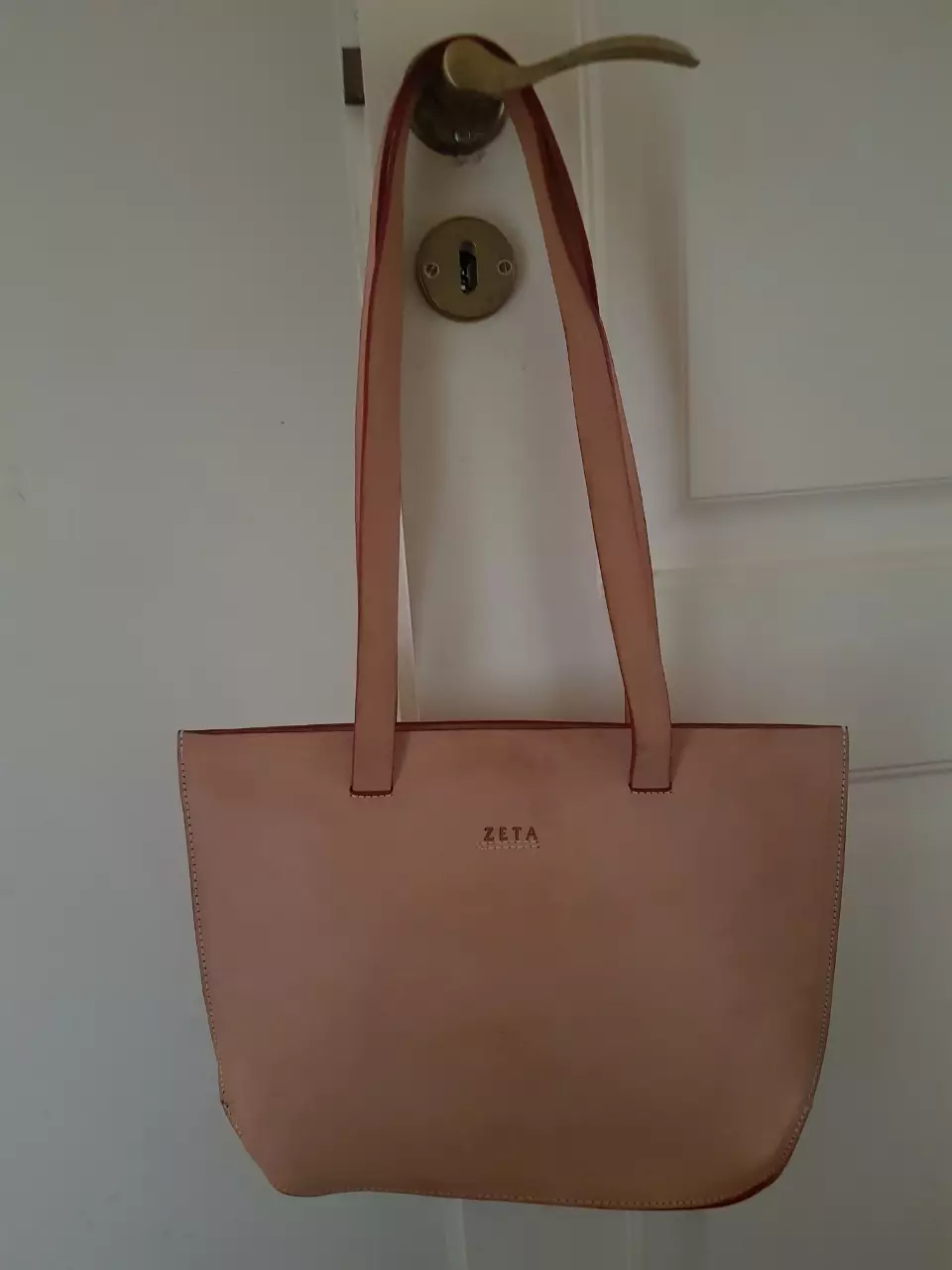 Bolso tote de cuero beige con el nombre de la marca 'ZETA' en la parte delantera. Ideal para llevar tus pertenencias con estilo y elegancia. Cuenta con un compartimento interno con cierre y forro a cuadros.