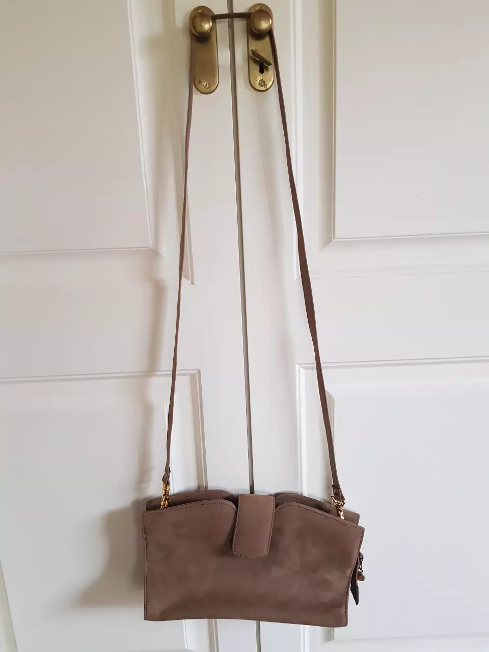 Cartera bandolera de gamuza marrón con solapa y cierre. Diseño elegante y funcional, ideal para llevar tus esenciales con estilo.