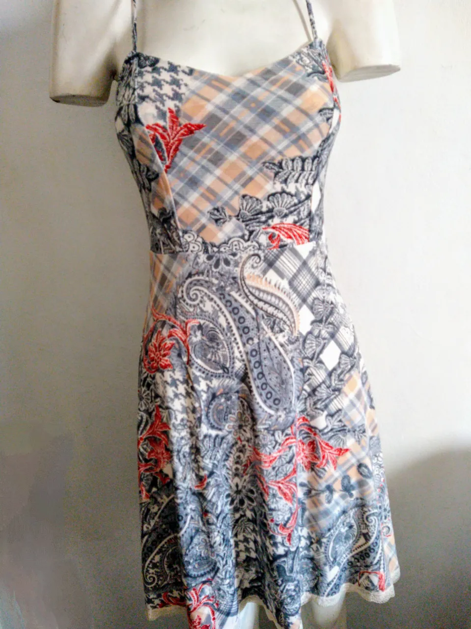 Vestido largo estampado con breteles finos y detalle de encaje en el ruedo. Posee un diseño patchwork con motivos de cuadros escoceses, paisleys y flores en tonos grises, rojos y crudos. La parte del busto es fruncida, lo que le da un toque canchero y cómodo.