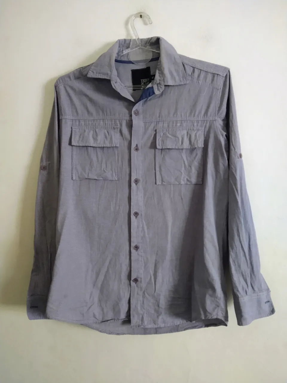 Camisa de manga larga de hombre, color gris con finas rayas blancas. Posee dos bolsillos en el frente, cuello clásico y la posibilidad de enrollar las mangas. Ideal para un look casual o para el trabajo.