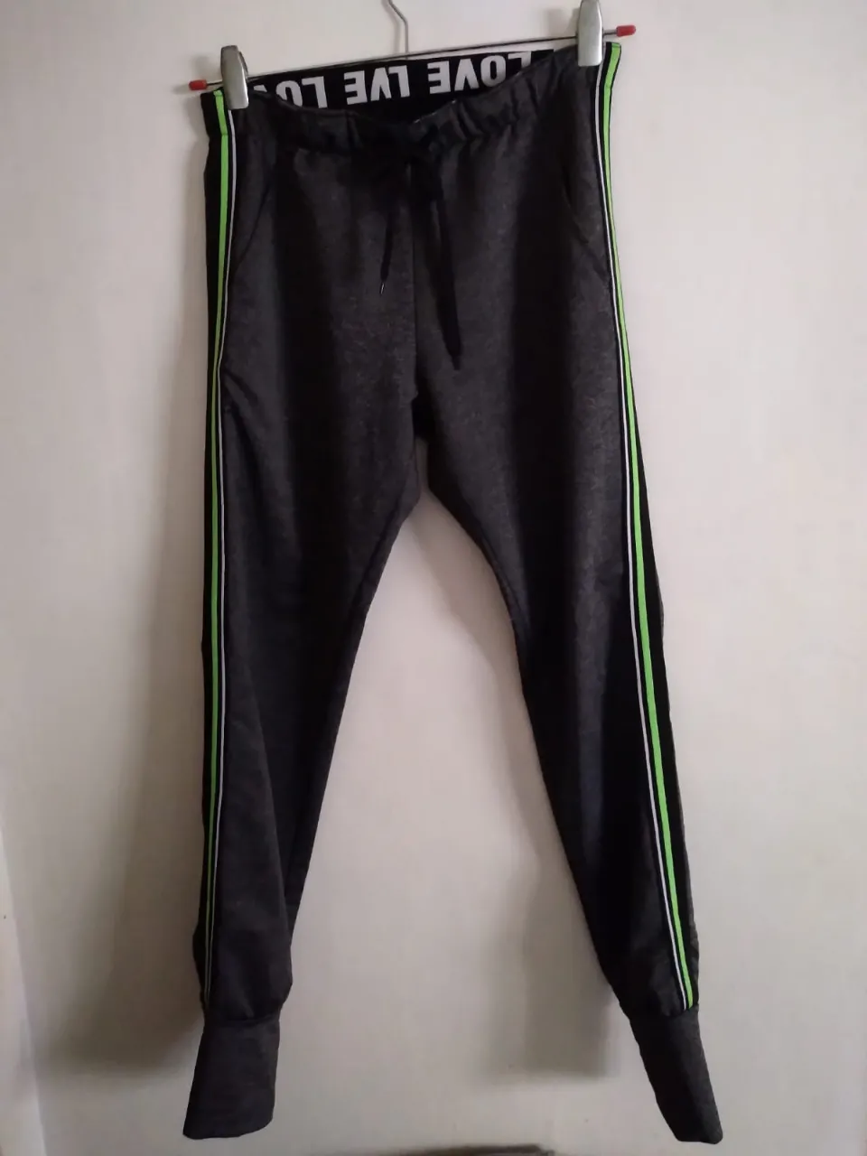 Pantalón importado, gris topo melange con líneas laterales en negro, verde neon y blanco. Cintura elastizada con cordón y estampa "LOVE LOVE LOVE". Ideal para entrenar o para un look casual y cómodo.