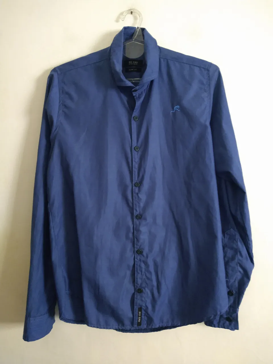 Camisa de vestir azul, manga larga, con un pequeño bordado de un animalito en el frente. Posee botones al tono y un corte slim fit.