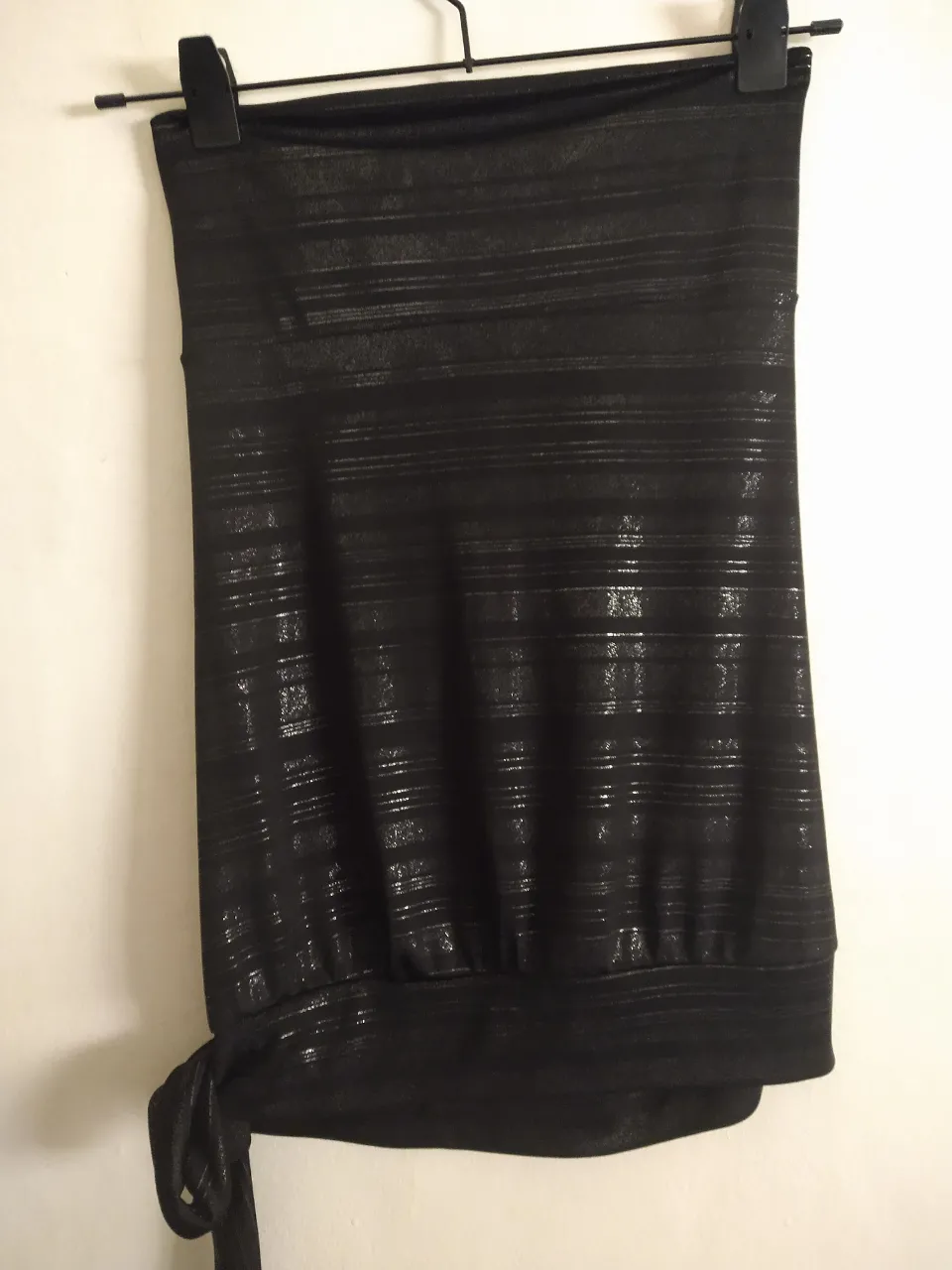 Top negro sin breteles con detalles de rayas plateadas brillantes. Tiene un lazo anudado en la parte inferior izquierda. Ideal para un look canchero y moderno.