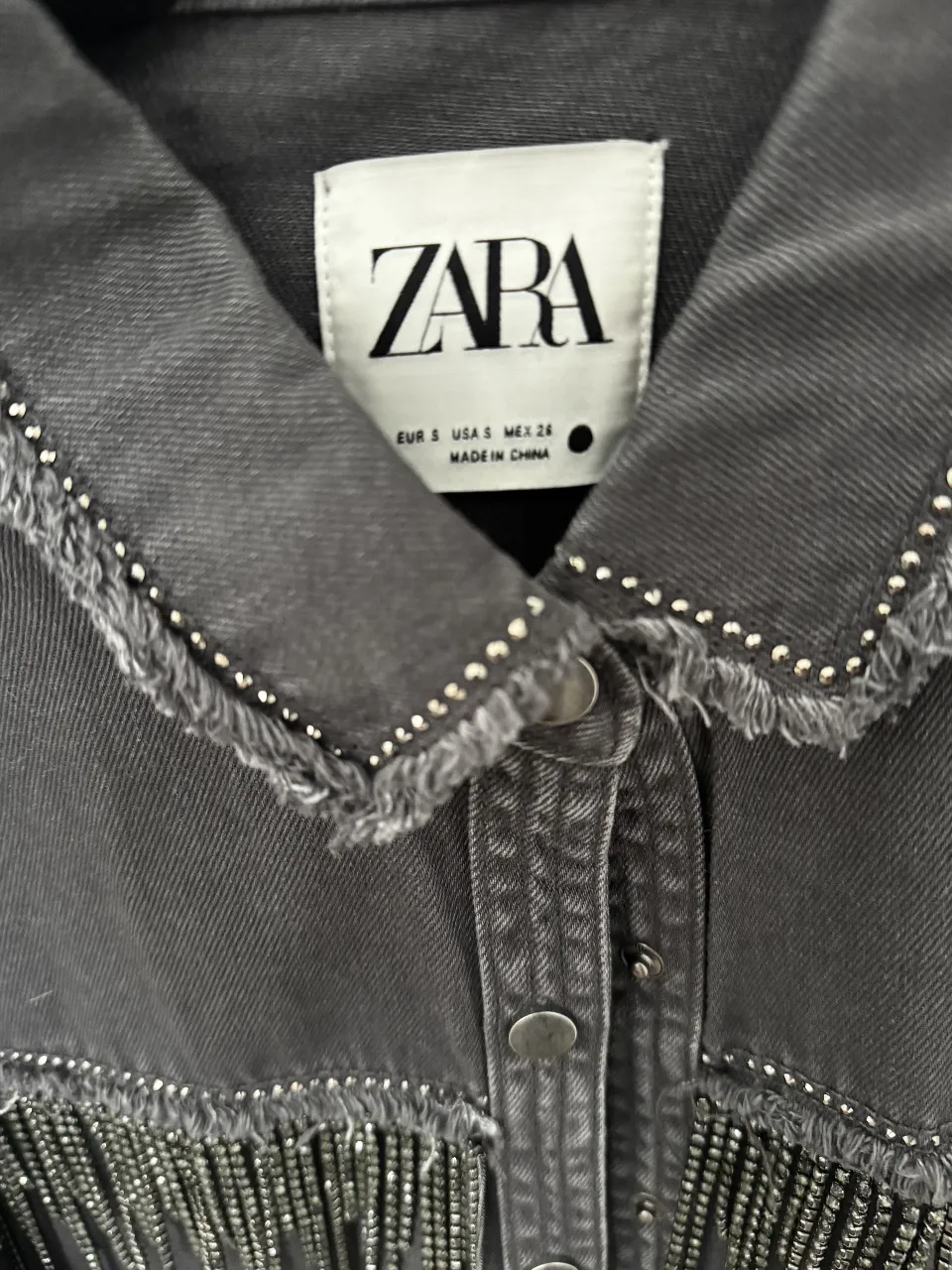 Campera de jean gris con detalles de flecos y tachas. Ideal para un look canchero y moderno. Talle S.
