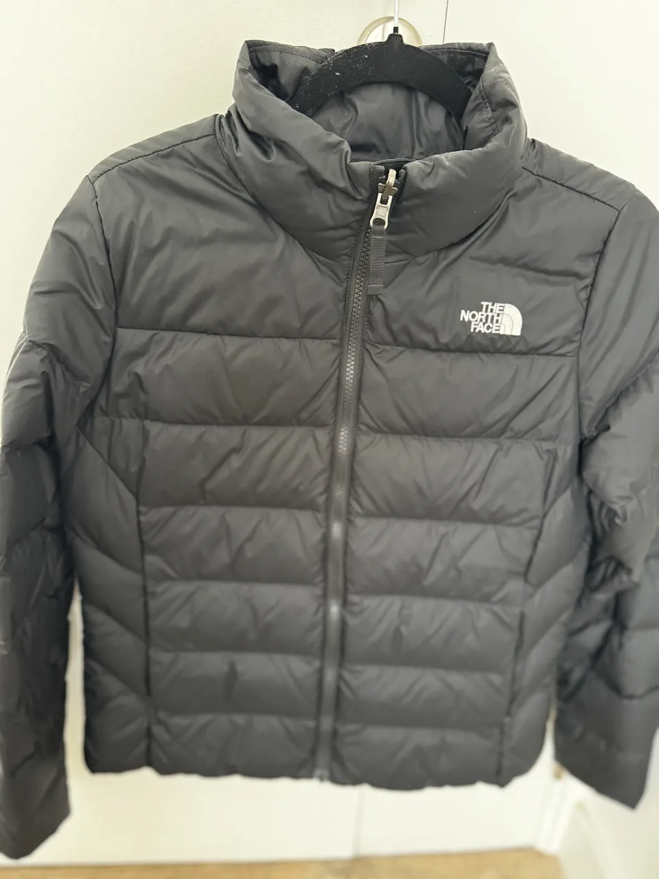 Campera de pluma The North Face negra para mujer, ideal para el invierno. Con cierre y cuello alto, perfecta para un look casual y abrigado.