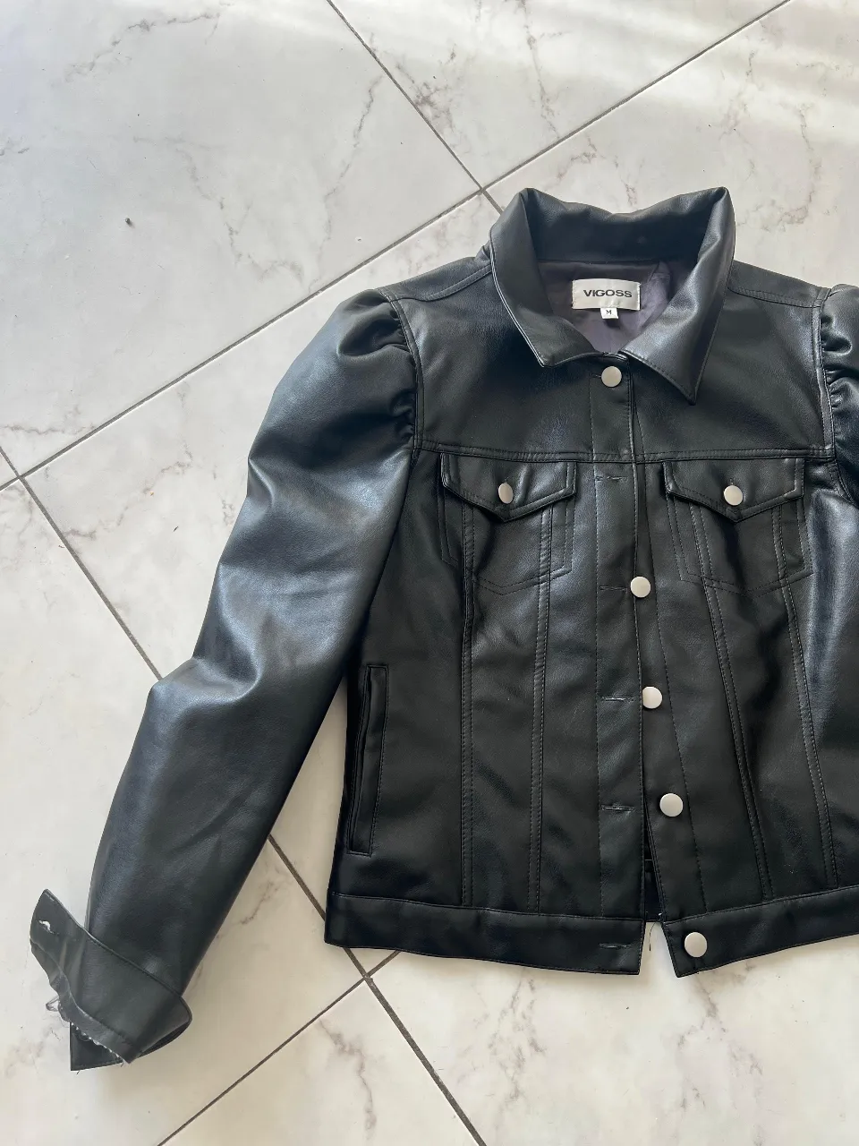 Campera biker de cuero sintético para mujer, con mangas abullonadas y detalles de botones plateados. Ideal para un look moderno y sofisticado.