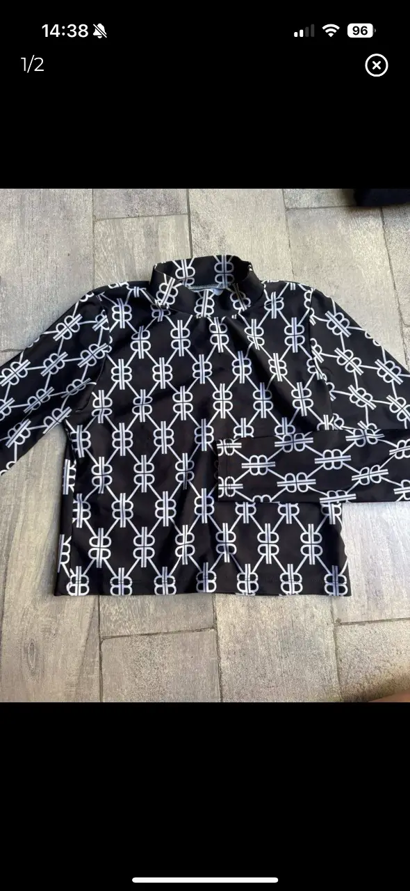 Blusa de mujer con estampado repetitivo de monograma en blanco y negro. Cuello alto y mangas largas. Ideal para un look elegante y moderno.