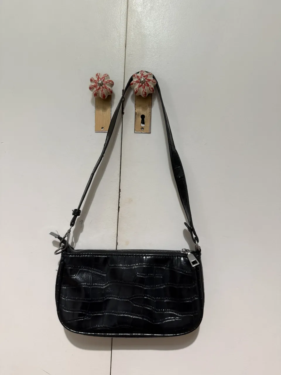 Cartera negra con textura de cocodrilo y cierre.