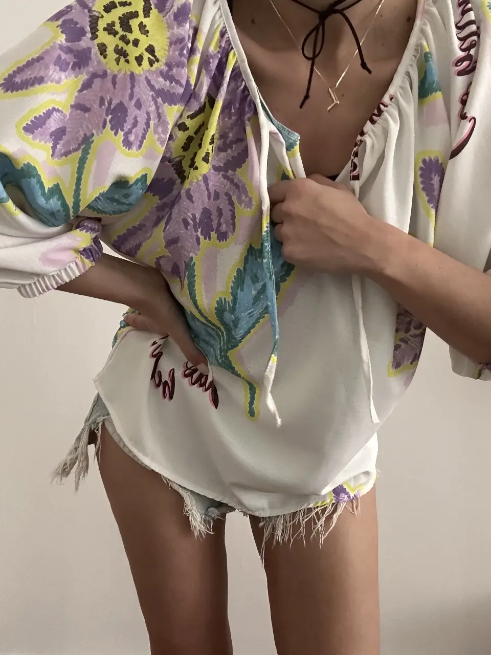 Blusa de mujer con estampado floral en tonos violetas, amarillos y celestes. Diseño holgado con mangas amplias y detalle de lazo en el cuello. Ideal para un look bohemio y fresco.