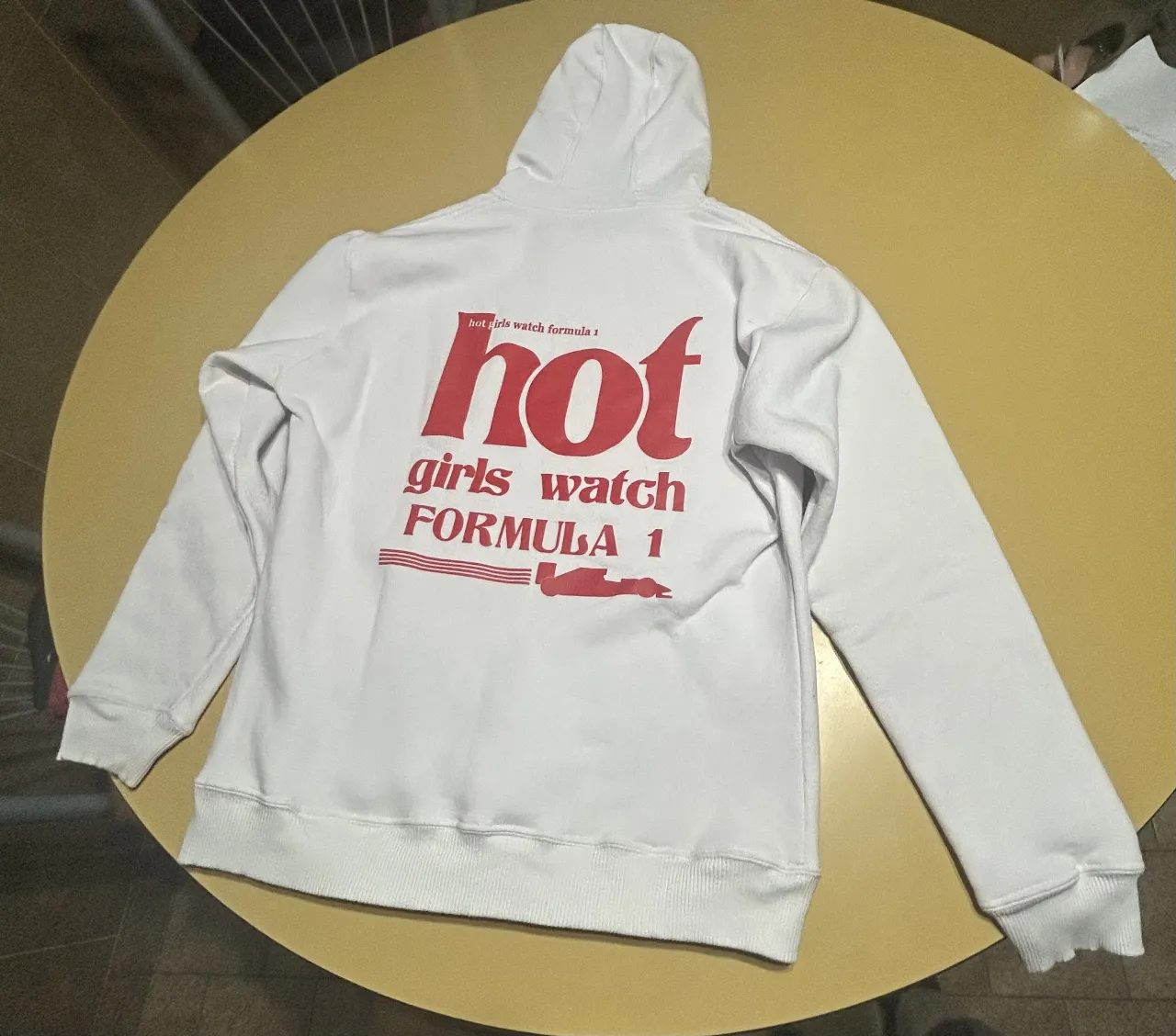 Buzo canguro blanco con capucha, con estampado "hot girls watch formula 1" en rojo en la espalda y el logo de formula 1 en el frente. Ideal para un look casual y moderno.