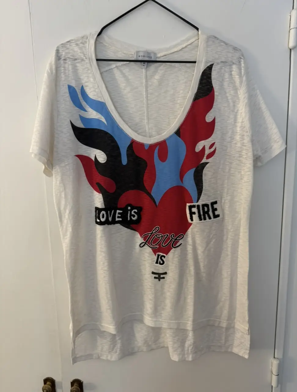 Remera blanca de algodón de Kosiuko con estampado de corazón en llamas y la frase "Love is Fire". Ideal para un look casual y con onda. poco uso!  
