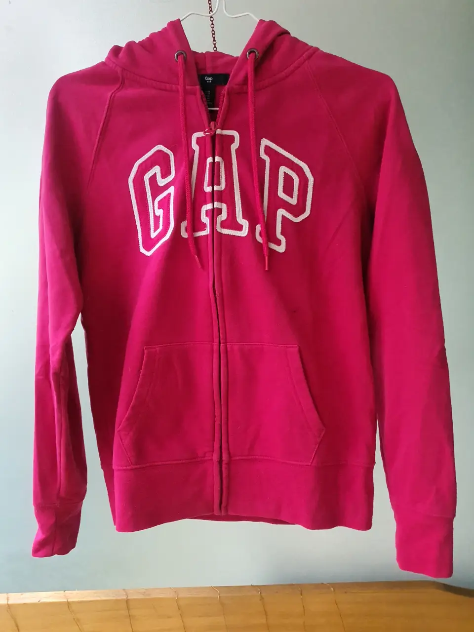 Buzo con cierre de la marca Gap, color rosa, con capucha y el logo de la marca en blanco. Talle XS.