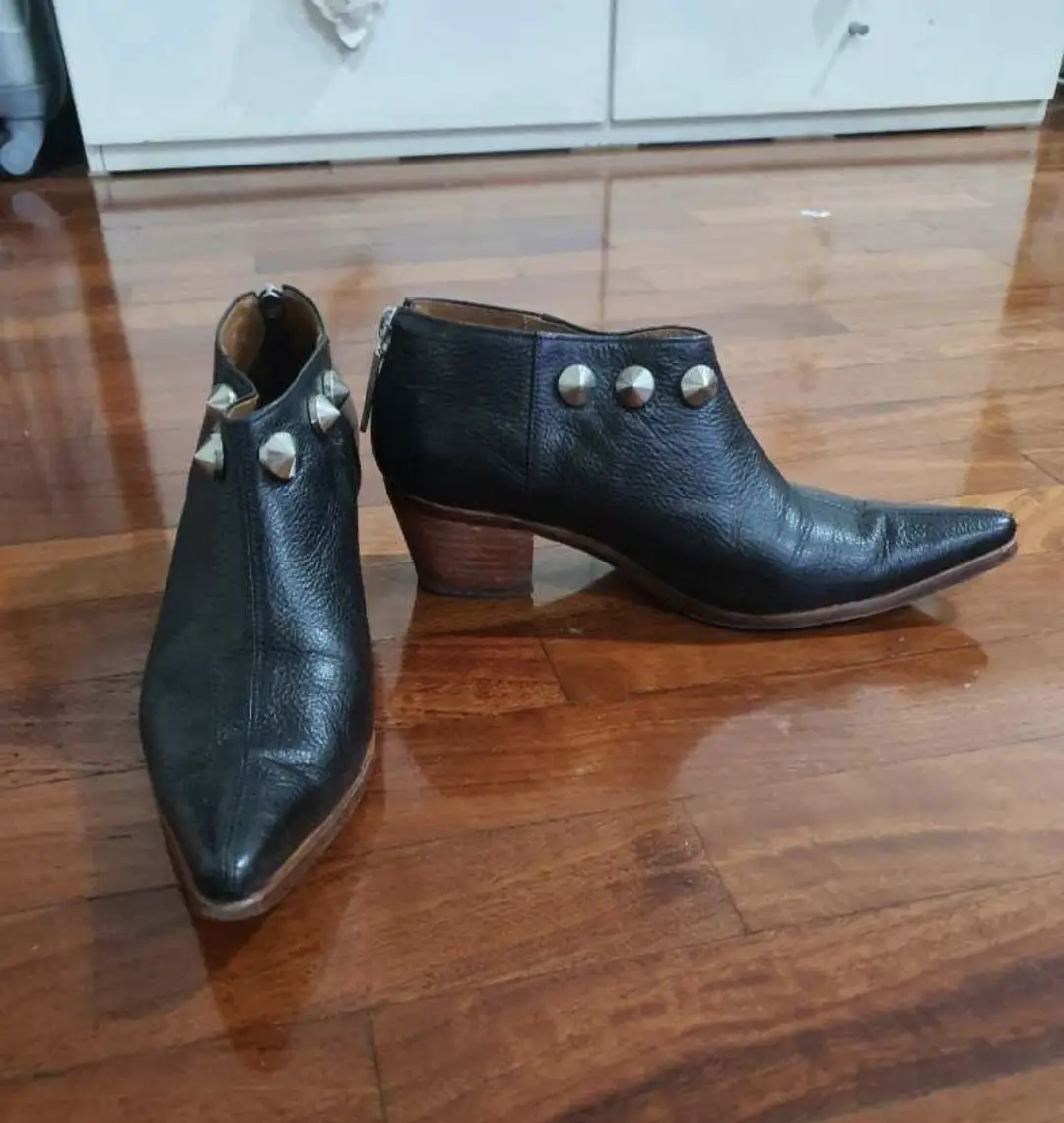 Botines de cuero negro con detalles de tachas plateadas. Diseño con punta fina y taco bajo de madera. Cierre trasero con detalle de cremallera. Son marca MIKI&CHOYA