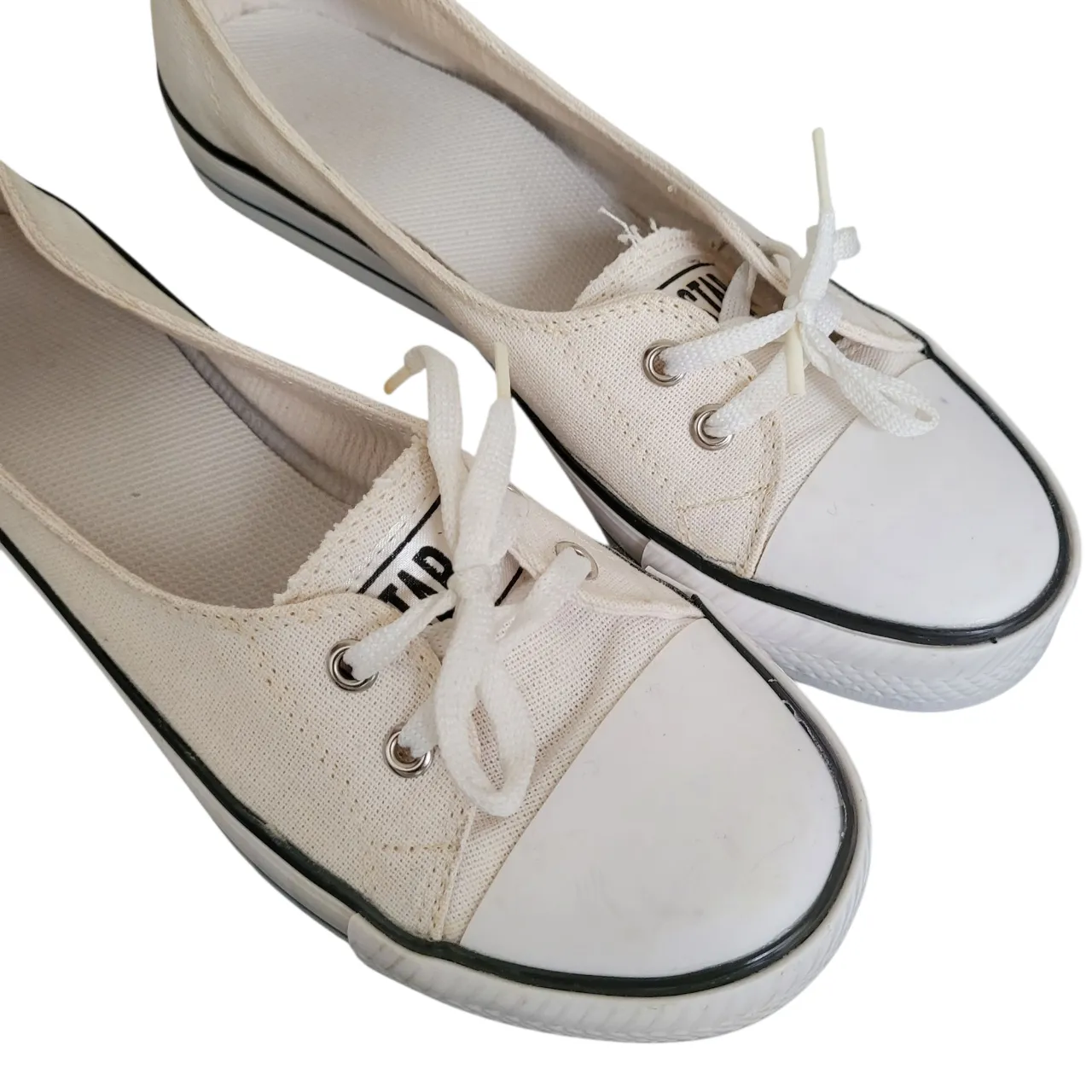 Zapatillas tipo ballerinas de lona blancas con cordones. Suela de goma negra con detalles. Ideales para un look casual y cómodo.