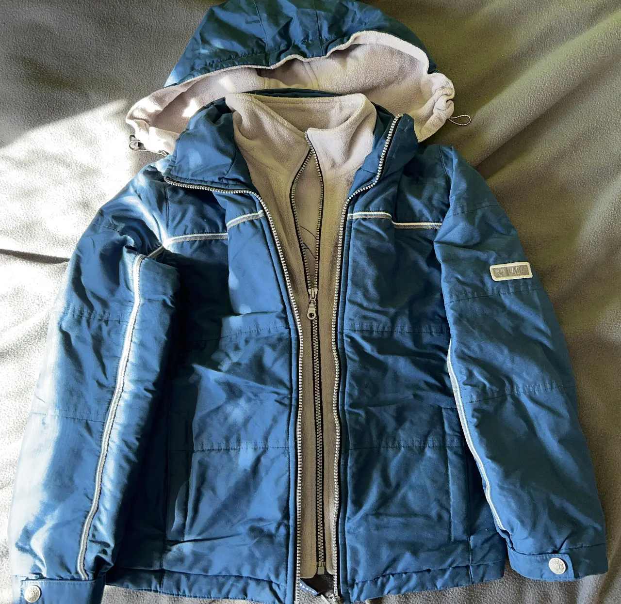 Campera deportiva azul con capucha desmontable y forro polar. Ideal para actividades al aire libre y deportes de invierno. Tiene doble cierre frontal y detalles en blanco.