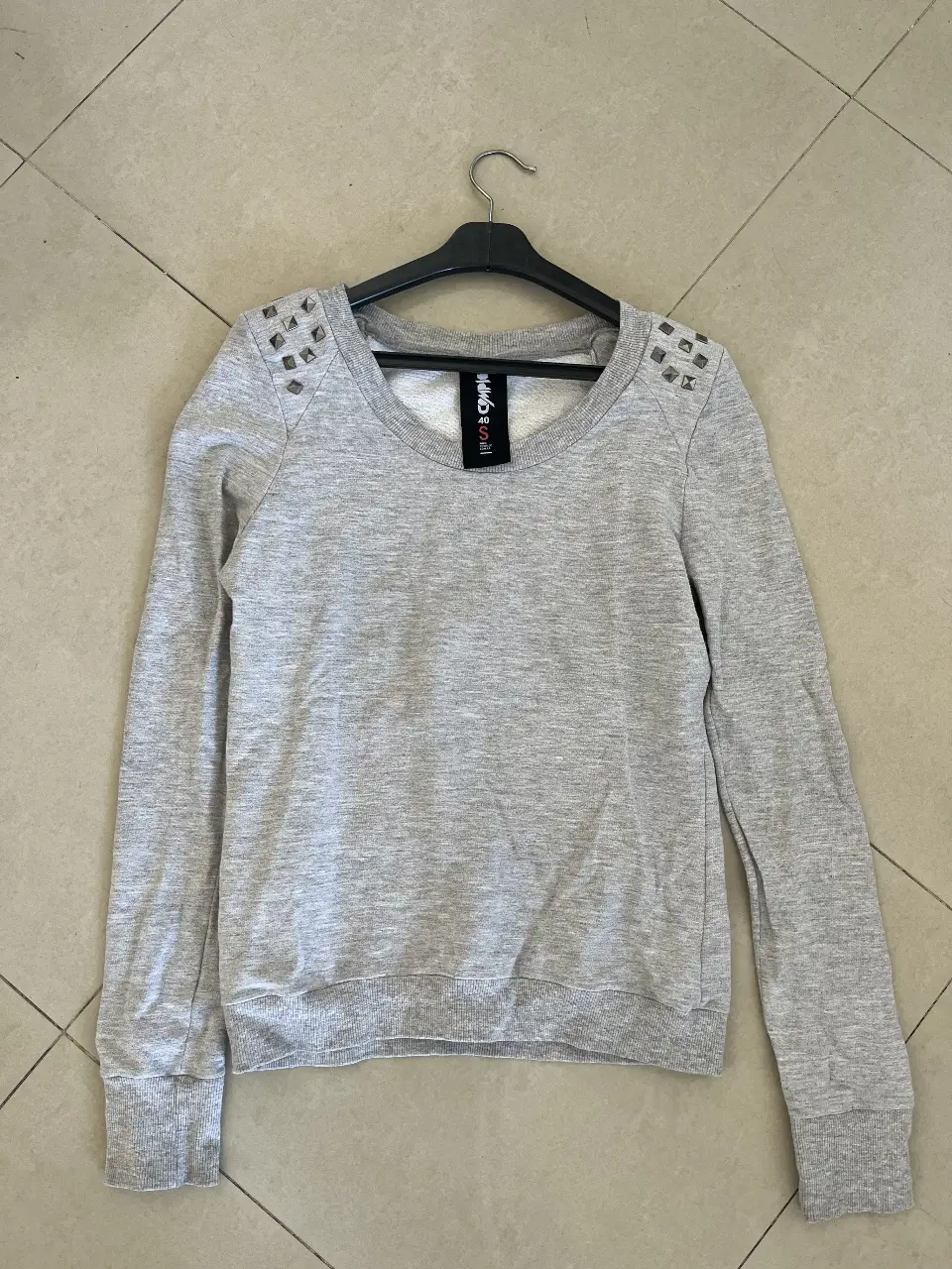 Buzo de cuello redondo gris con detalles de tachas en los hombros. Ideal para un look casual y canchero.