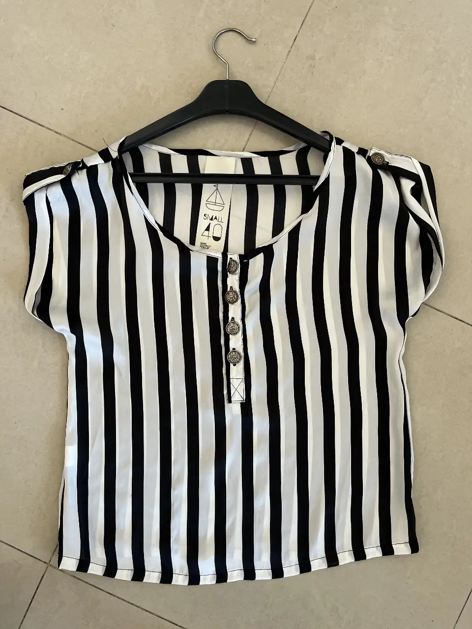 Blusa a rayas verticales en blanco y negro, con botones y detalles en los hombros. Ideal para un look casual y elegante.