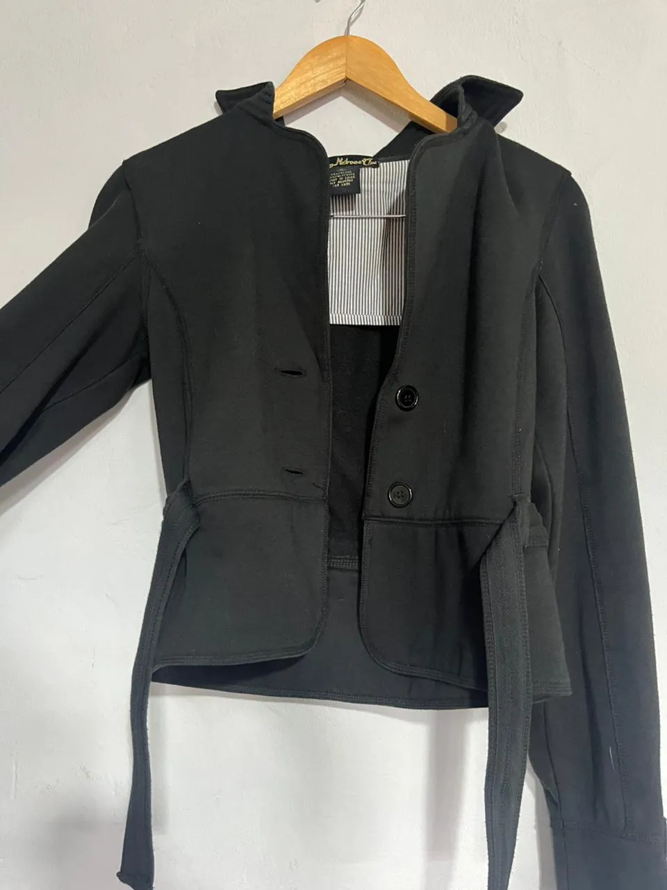 Chaqueta negra entallada con cinturón, ideal para un look canchero y moderno. Perfecta para usar abierta o cerrada, con botones al frente y un cuello distintivo. Combina estilo y comodidad para el día a día.