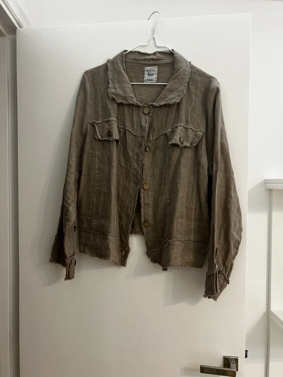 Campera de lino color marrón con cuello solapa, botones al frente y dos bolsillos superiores con tapa. Posee detalles deshilachados en puños, cuello y ruedo.