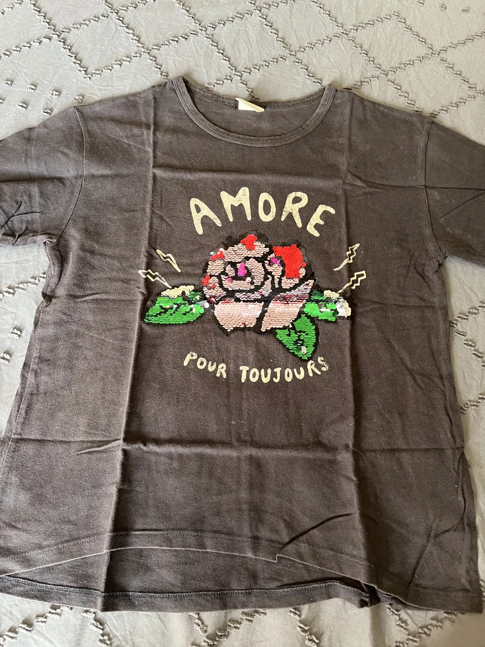 Remera gris oscura con estampa de "AMORE POUR TOUJOURS" y un diseño de flor con lentejuelas. Ideal para un look casual y divertido.