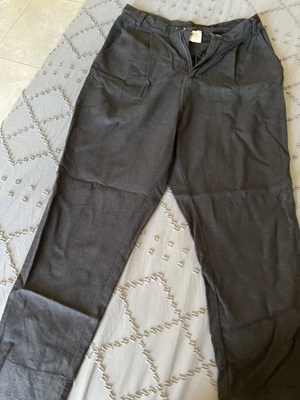 Pantalón negro de vestir, tiro alto, con bolsillos y detalles de pinzas. Ideal para un look elegante y moderno.  