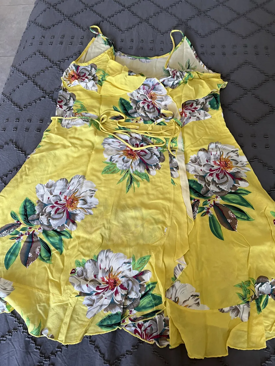 Vestido amarillo vibrante con un estampado floral grande y llamativo. Diseño con tirantes finos, volados en el escote y un lazo para anudar en la cintura. Ideal para un look fresco y femenino en días soleados.
