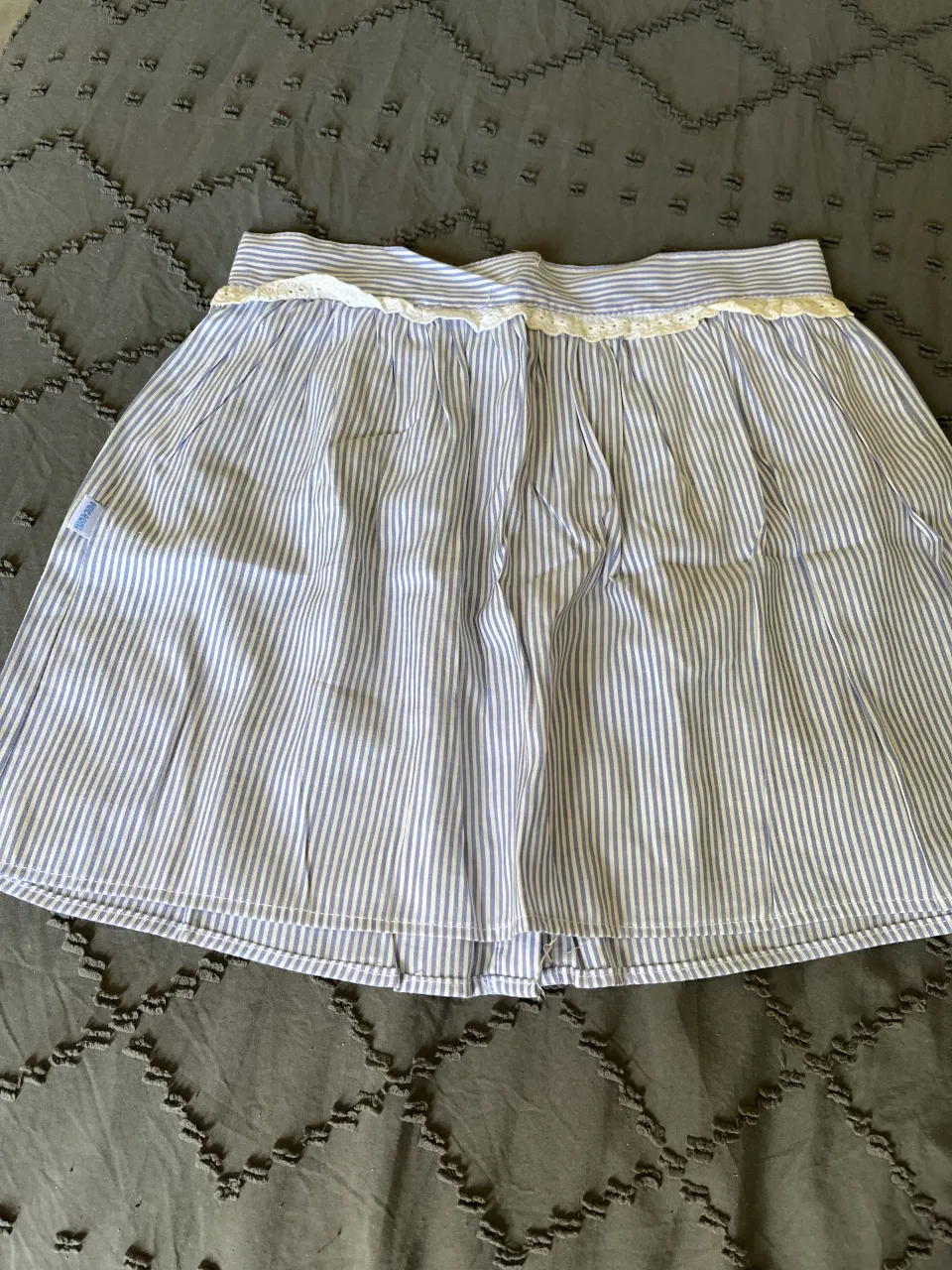 Pollera a rayas celestes y blancas, con detalles de puntilla en la cintura y botones al frente. Ideal para un look casual y fresco.