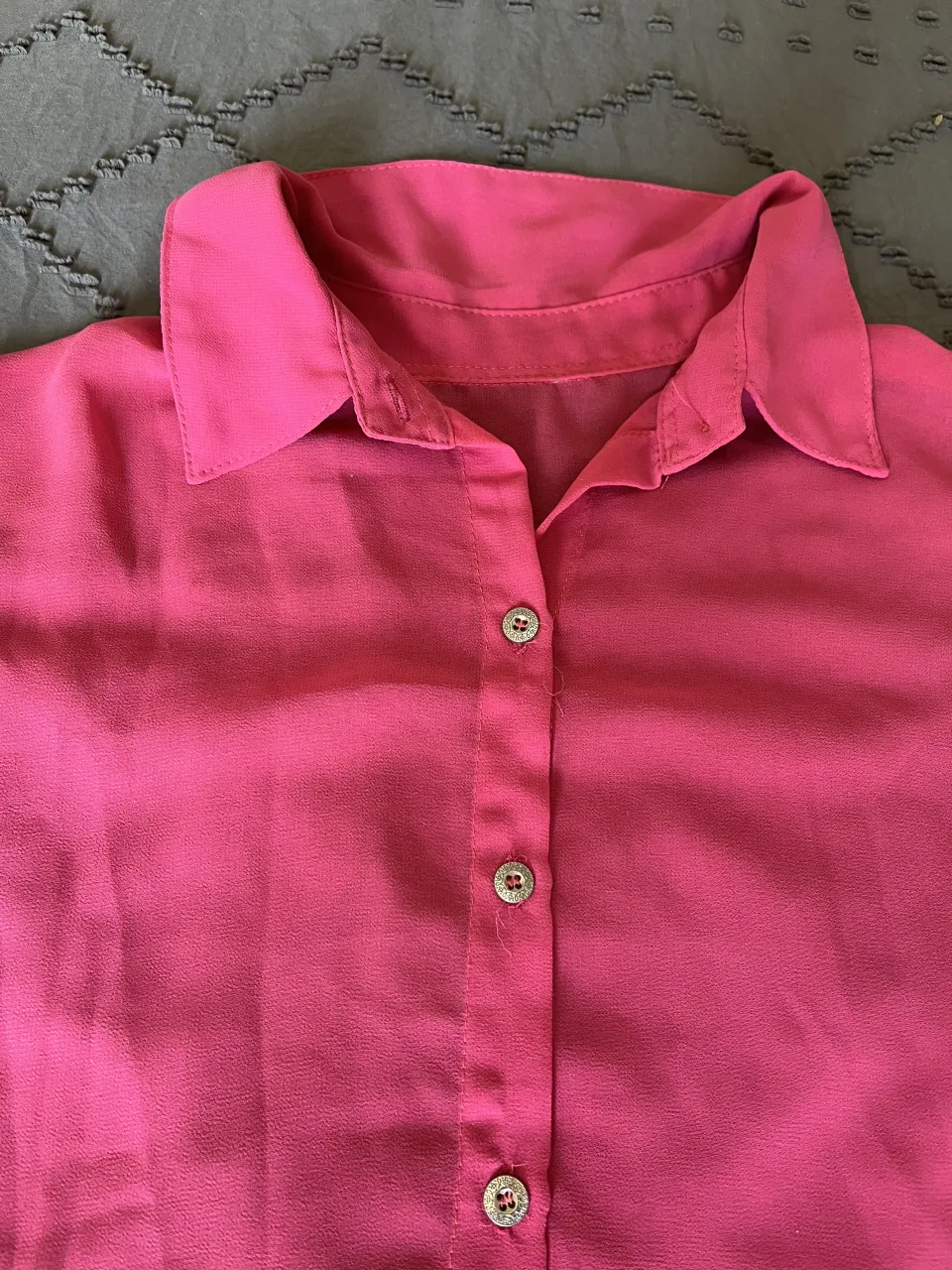 camisa rosa vibrante con cuello camisero y botones al frente. Diseño moderno con mangas cortas y un corte asimétrico en la parte inferior, más larga atrás. Ideal para un look casual y chic.