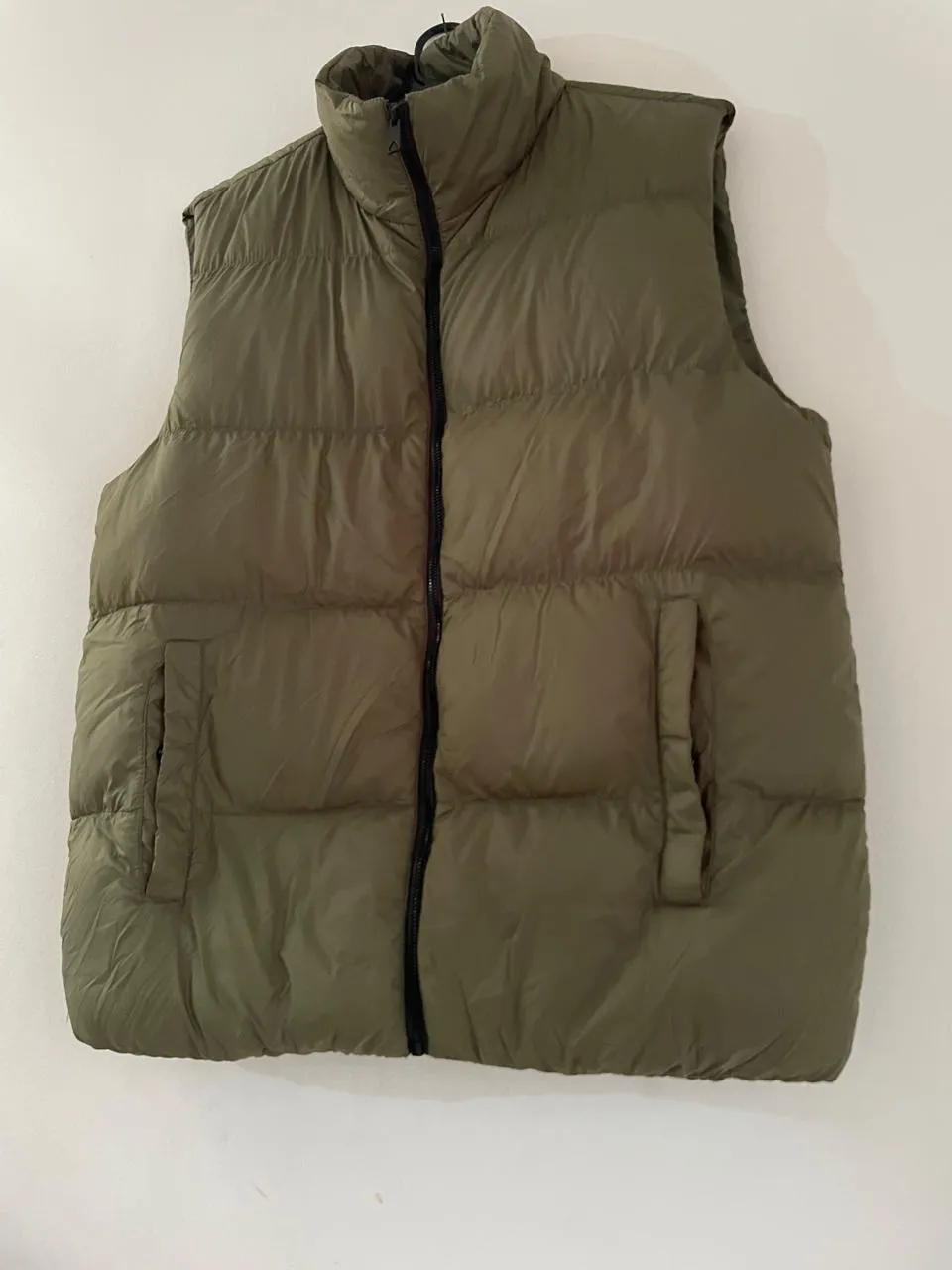 Chaleco acolchado de color verde militar con cierre completo al frente y bolsillos laterales con botón a presión.