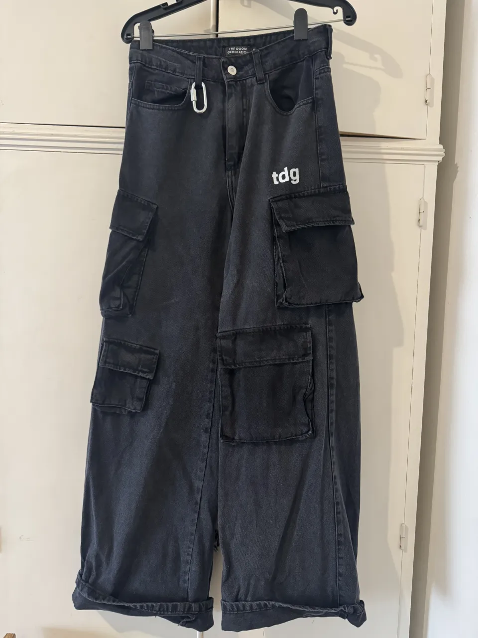 Pantalón cargo de jean color gris oscuro con múltiples bolsillos. Estampa de logo blanco en la parte superior izquierda.