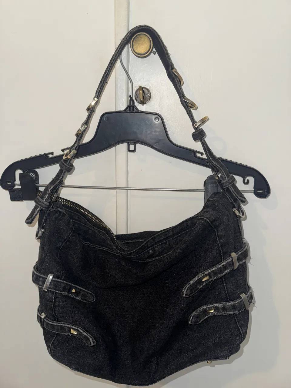 Bolso de jean negro con múltiples hebillas y detalles metálicos. Cierre principal superior y correa ajustable.