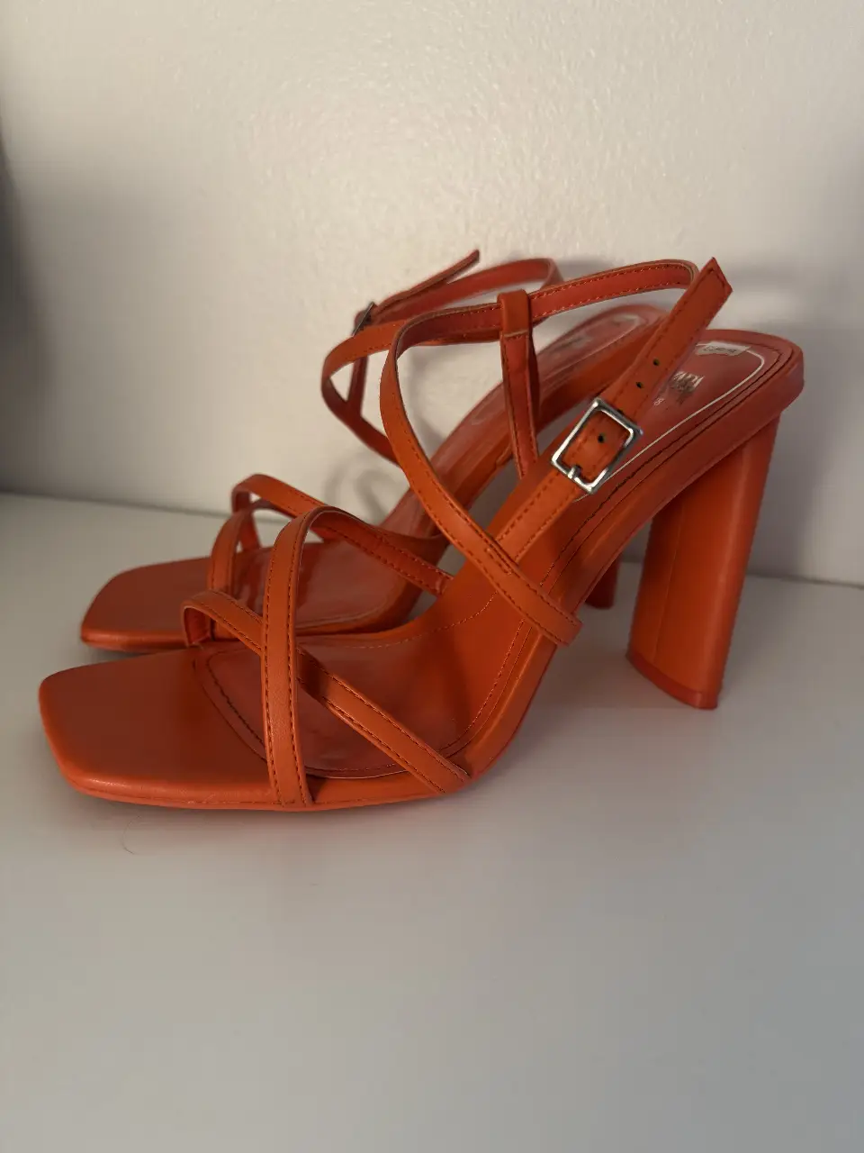 Sandalias naranjas con taco ancho y tiras cruzadas. Ideales para un look moderno y elegante.