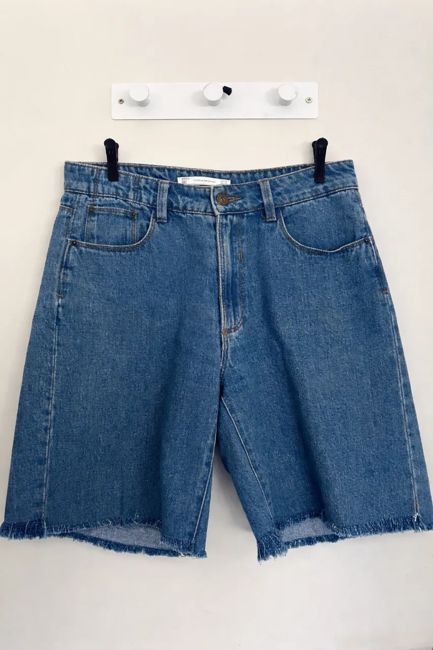 Shorts de jean de tiro alto con roturas y flecos en el ruedo. Cierre con botón y bolsillos.