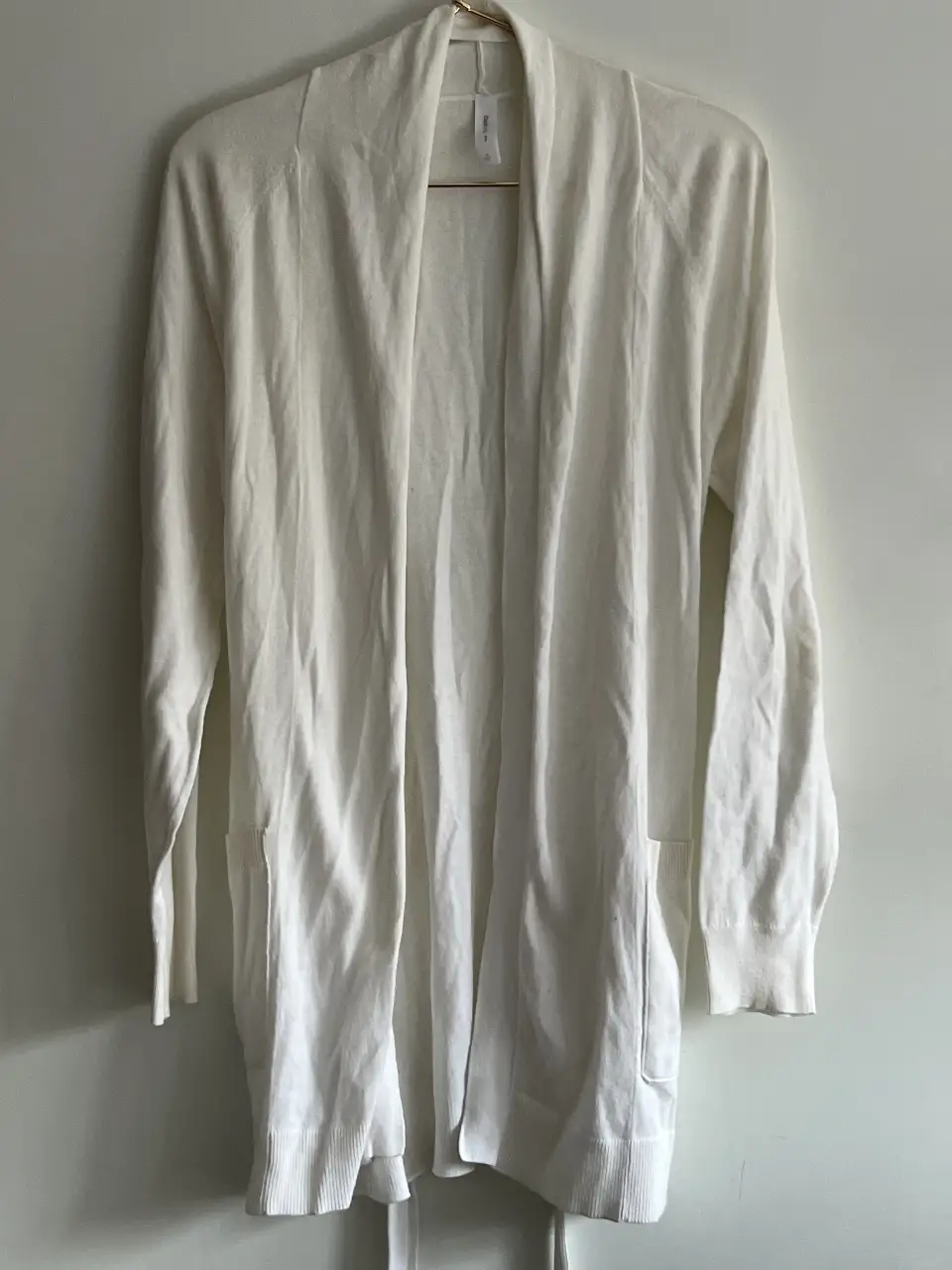 Cardigan largo de mujer, color blanco, con bolsillos delanteros y cinturón para ajustar en la cintura. Ideal para un look casual y cómodo.