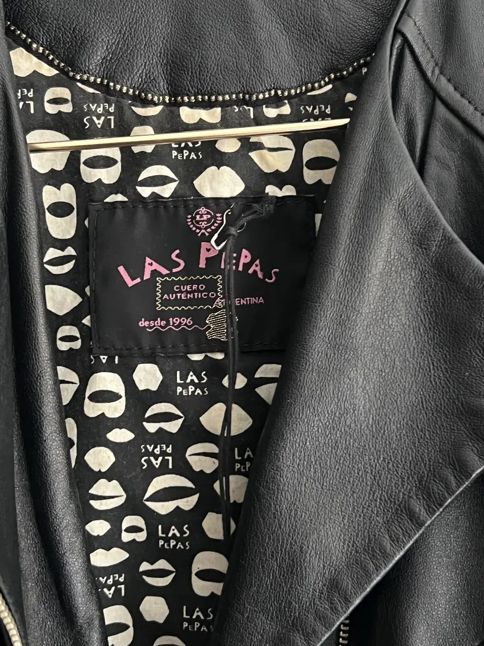 Campera biker de cuero sintético negro de la marca Las Pepas. Con detalles de cierre en los bolsillos y en las mangas. Interior con estampado de labios.
