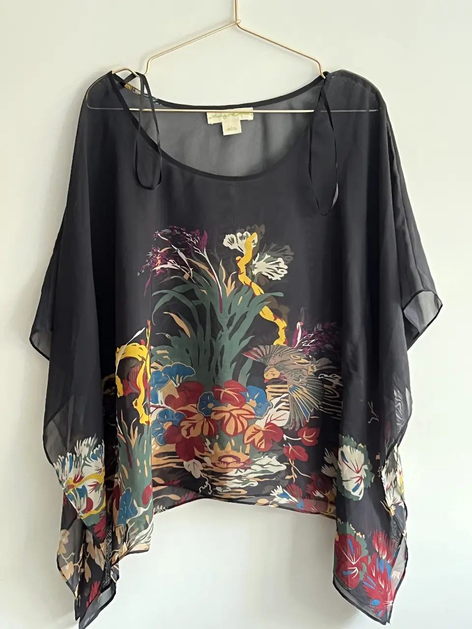 Blusa negra de gasa con estampado floral. Tiene mangas amplias y lazos en los hombros. Ideal para un look bohemio y elegante.