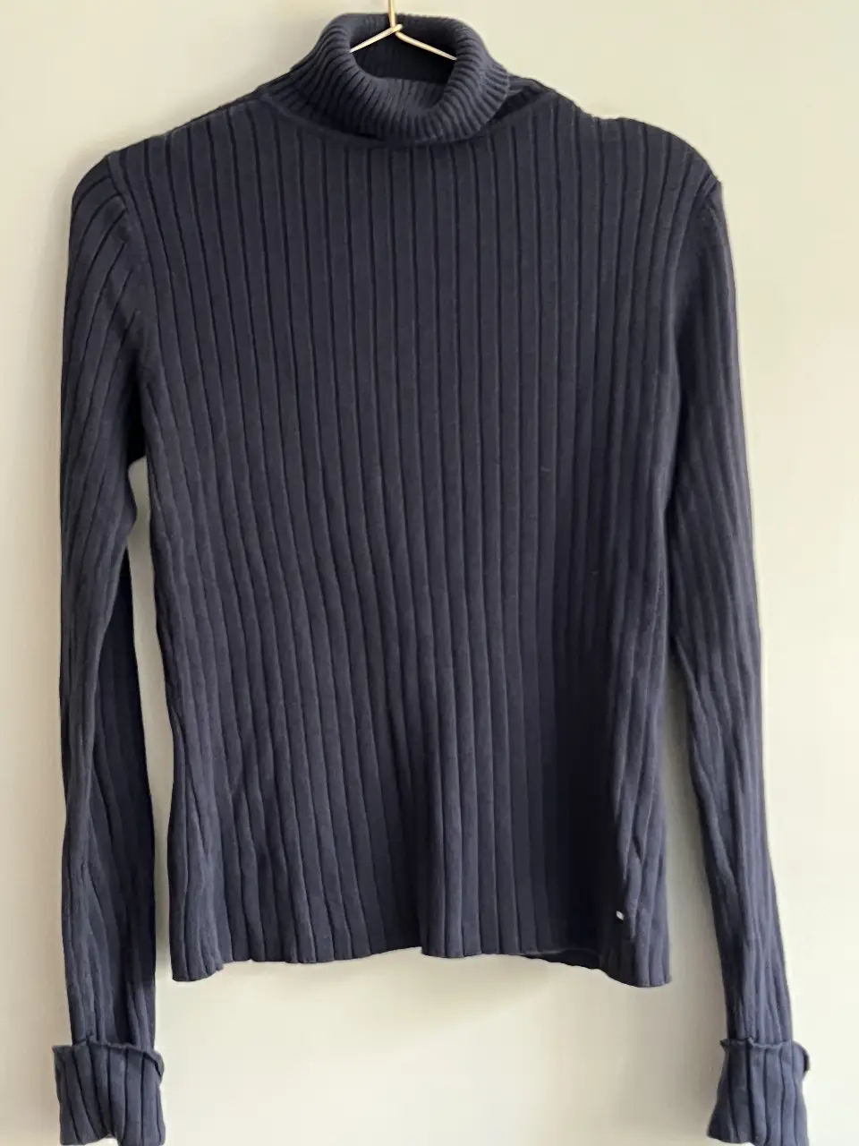 Sweater de cuello alto de mujer, de color azul marino. Confeccionado en tejido de punto acanalado, con mangas largas y puños con detalle de vuelta. Ideal para un look casual y abrigado.