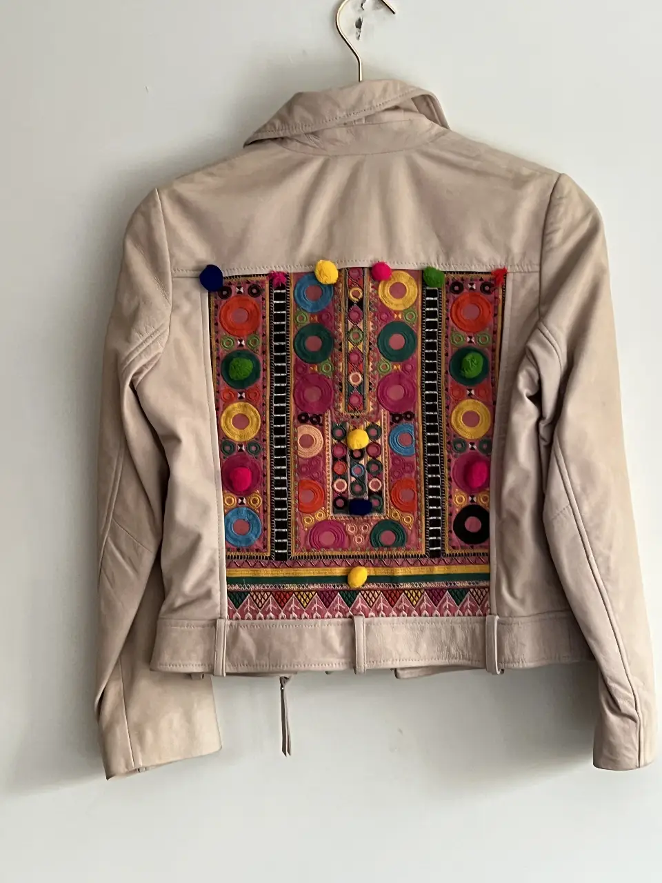 Campera de cuero sintético color crudo con detalles bordados en la espalda. Posee cierre y bolsillos con cremalleras. Ideal para un look casual y canchero.