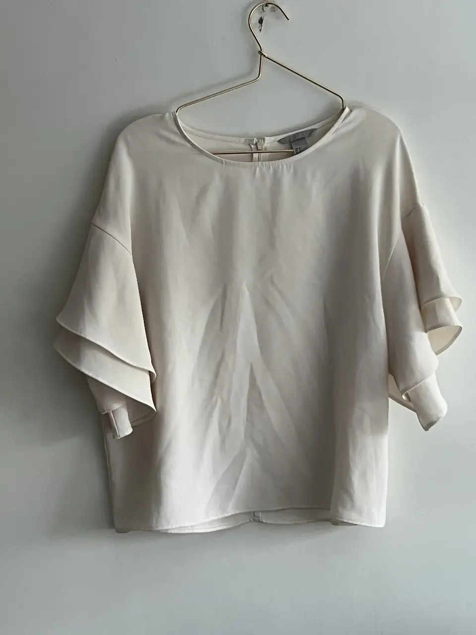Blusa de mujer color blanco roto, con mangas cortas con volados y cierre en la espalda. Ideal para un look elegante y fresco.