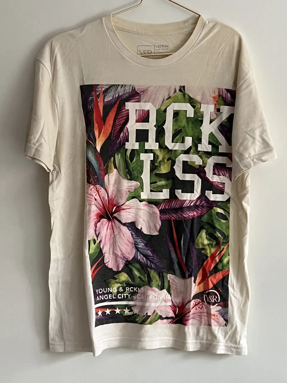 Remera de hombre color crudo con estampado floral y la palabra "RECKLESS" en blanco. Ideal para un look casual y moderno.