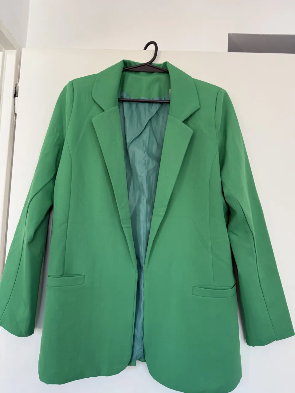 Conjunto de blazer y shorts color verde. El blazer es de corte clásico con solapas y bolsillos frontales. Los shorts son tiro alto con lazo para atar a la cintura y dobladillo en la parte inferior.
