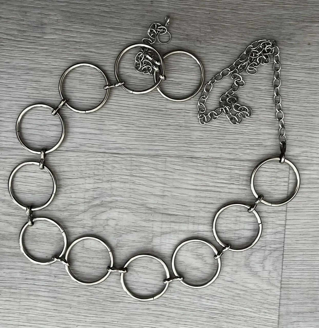 Cinturón plateado con cadena y aros grandes.