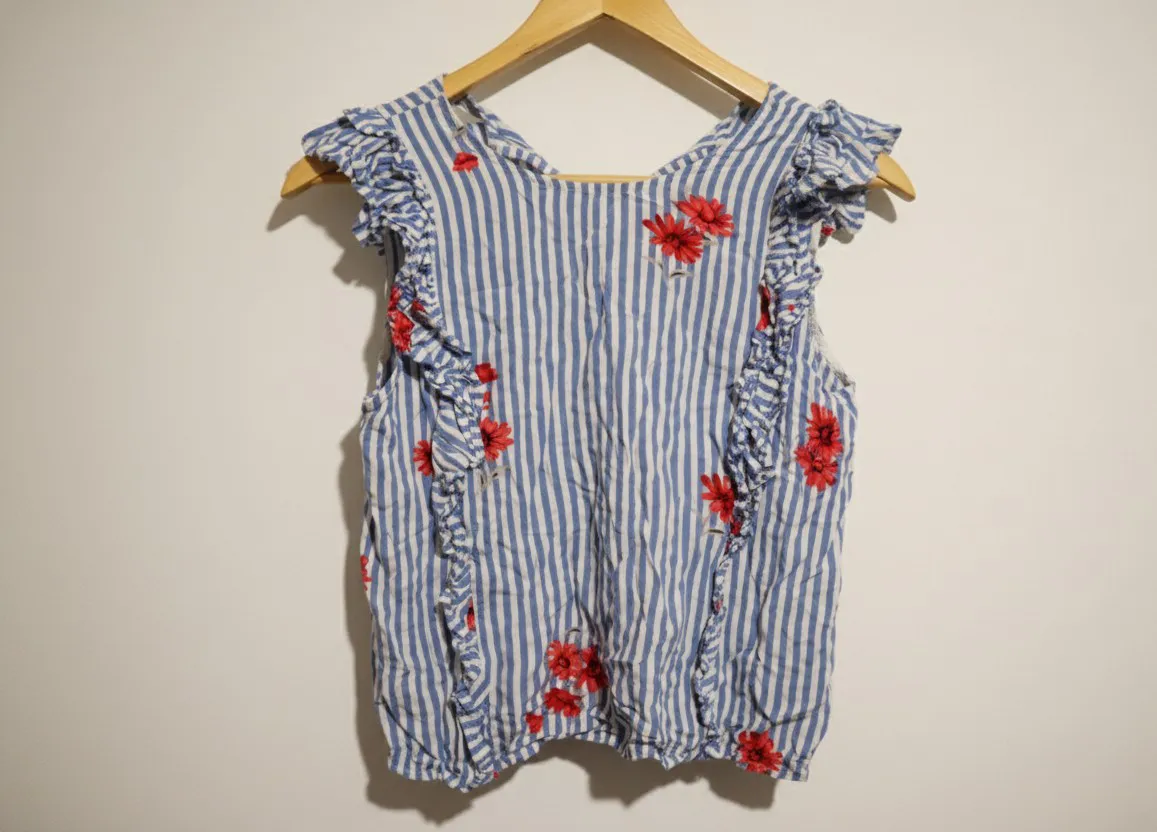 Remera de mujer a rayas verticales azules y blancas con estampa de flores rojas. Tiene volados en las mangas y en los laterales. Ideal para un look fresco y casual.